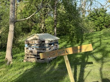 A bug hotel made of stacked wooden pallets and natural materials in a grassy area with a wooden sign reading bug hotel vacancies at The Farmhouse in Newport Pembrokeshire