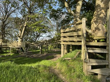 An outdoor wooden climbing structure and walkway among trees in a grassy area at The Farmhouse in Newport Pembrokeshire