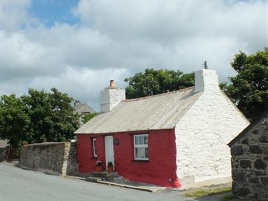 A small red and white cottage with two chimneys on a road with green trees at Bwthyn Alarch in Trefin St Davids Pembrokeshire