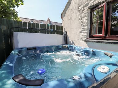 An outdoor hot tub beside a white stone wall with a wooden fence in the background at Bwthyn Alarch in Trefin St Davids Pembrokeshire