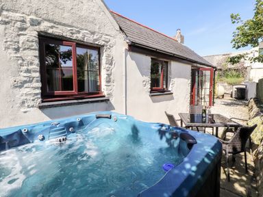 An outdoor patio with a bubbling hot tub a glass table with four woven chairs and a bottle with glasses at Bwthyn Alarch in Trefin St Davids Pembrokeshire