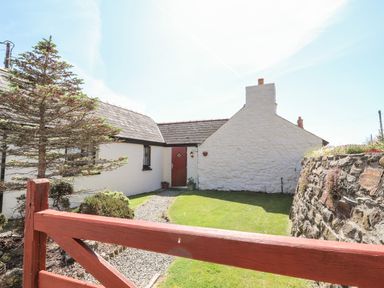 A small white cottage with a red door a gravel path green lawn and a red wooden gate at Bwthyn Alarch in Trefin St Davids Pembrokeshire