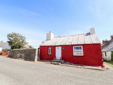 A red stone cottage with a white door and window next to a stone wall at Bwthyn Alarch Trefin St Davids Pembrokeshire
