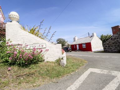 A red and white cottage near a street sign with pink flowers at Pwllan in Trefin St Davids Pembrokeshire
