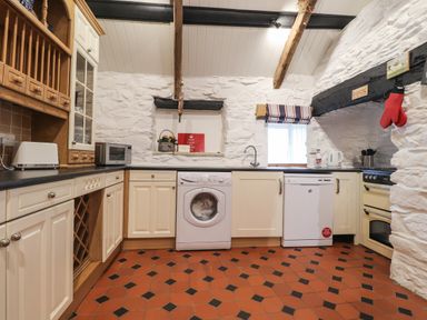 A kitchen with white cabinets, washing machine, dishwasher, microwave, toaster, stove, and tiled floor at Bwthyn Alarch in Trefin St Davids Pembrokeshire