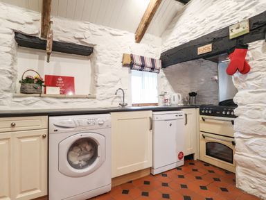 A kitchen with white appliances wooden cabinets and stone walls at Bwthyn Alarch in Trefin St Davids Pembrokeshire