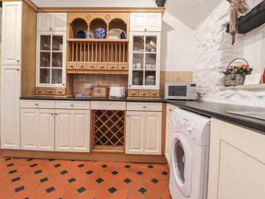 A kitchen with cabinets a washing machine a microwave and decorative items at Bwthyn Alarch in Trefin St Davids Pembrokeshire