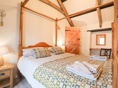 A bedroom with a wooden four-poster bed bedside table with lamp towels on the bed and a wooden door at Bwthyn Alarch in Trefin St Davids Pembrokeshire