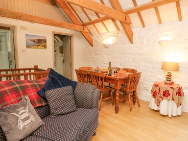A dining area with a wooden table and chairs next to a sofa with cushions and a small table with a lamp at The Granary in Newport Pembrokeshire