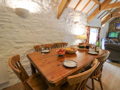 A wooden dining table with six chairs plates glasses fruit and cheese in a room with white stone walls and wooden beams at The Granary in Newport Pembrokeshire