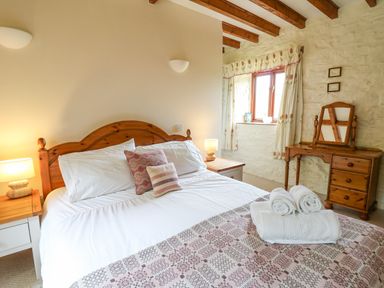 A bedroom with a wooden bed white bedding two bedside tables with lamps a wooden dressing table and a window with curtains at The Granary in Newport Pembrokeshire