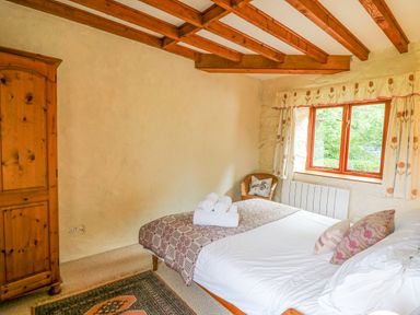 A bedroom with a bed folded towels wooden wardrobe window and chair at The Granary in Newport Pembrokeshire