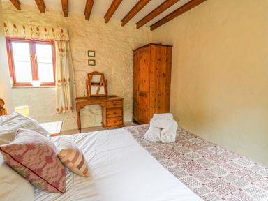 A bedroom with a bed pillow and towels by a window with curtains a wooden dressing table and wardrobe at The Granary in Newport Pembrokeshire