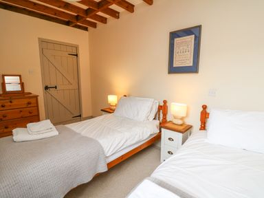 A bedroom with two single beds bedside tables with lamps a wooden dresser and a wooden door at The Granary in Newport Pembrokeshire