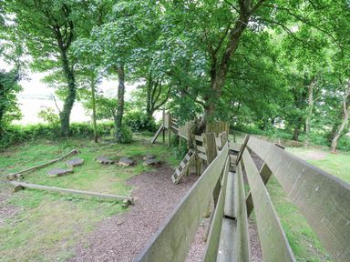 An outdoor playground area with wooden play structures and tree stumps among green trees at The Granary in Newport Pembrokeshire