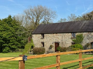 A stone house with a black roof and wooden fence on a grassy lawn with trees in the background at The Granary in Newport Pembrokeshire