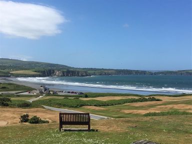 A bench on grassland overlooking a beach with cliffs and the sea at Stable Cottage in Newport Pembrokeshire