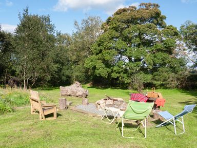 An outdoor seating area with wooden benches chairs a fire pit and trees in the background at Stable Cottage in Newport Pembrokeshire