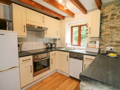 A kitchen with cream cabinets wooden beams and a stone wall at Stable Cottage in Newport Pembrokeshire