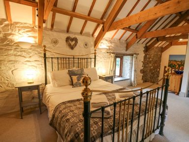 A bedroom with a metal bed frame exposed wooden beams and stone walls at Stable Cottage in Newport Pembrokeshire