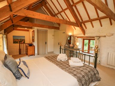 A bedroom with a wooden beamed ceiling a bed with folded towels a dresser with a mirror and a window at Stable Cottage in Newport Pembrokeshire