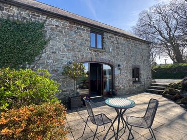 A stone building with a small patio featuring a round table and two chairs at Stable Cottage in Newport Pembrokeshire