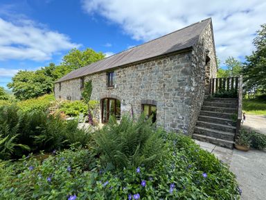 A stone cottage with a slate roof surrounded by plants and flowers with stairs on the side at Stable Cottage in Newport Pembrokeshire