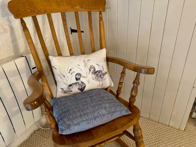 A wooden rocking chair with two cushions by a white radiator and paneled wall at Stable Cottage in Newport Pembrokeshire