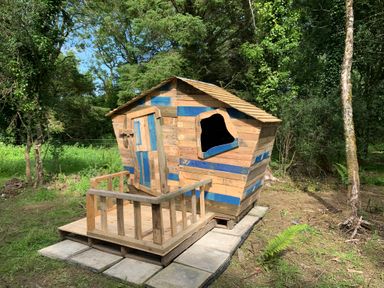 A small wooden playhouse with a porch in a forest clearing at Stable Cottage in Newport Pembrokeshire