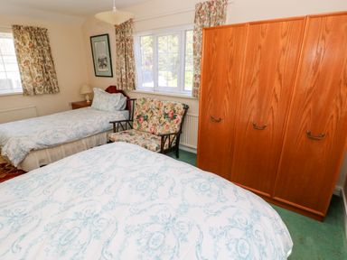 A bedroom with two single beds a floral patterned sofa a wooden wardrobe and windows with floral curtains at Otter Cottage in Dinas Cross