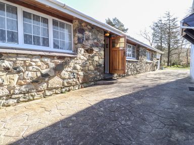 Stone cottage exterior with three white framed windows and an open wooden door on a paved path at Otter Cottage in Dinas Cross