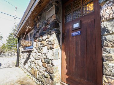 A stone exterior wall with a wooden door labeled Otter and a hanging basket at Otter Cottage in Dinas Cross