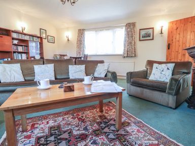 A living room with sofas coffee table bookshelf and window at Otter Cottage in Dinas Cross