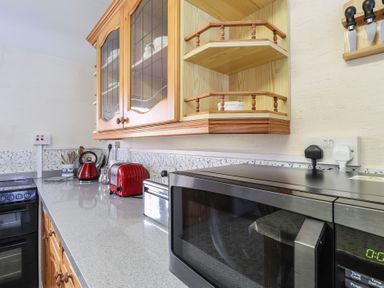 A kitchen countertop with a microwave oven toaster kettle and glass-fronted wooden cabinets at Otter Cottage in Dinas Cross