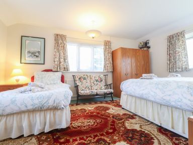 A bedroom with two single beds a floral sofa a wooden wardrobe and patterned curtains at Otter Cottage in Dinas Cross
