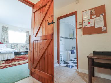An open wooden door leading to a bedroom with a bed and floral sofa and a bathroom with a bathtub and checkered floor at Otter Cottage in Dinas Cross