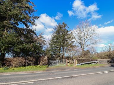 A roadside view of metal and wooden gates with trees and bushes behind at Otter Cottage in Dinas Cross