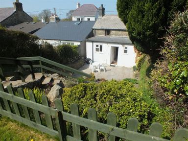 A garden area with green bushes wooden fence stone steps and a small patio with white chairs and table at Derlwyn in Newport Pembrokeshire