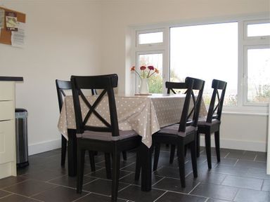 A dining area with a table covered by a polka dot tablecloth and six black chairs near large windows at Gellifor in St Dogmaels Pembrokeshire