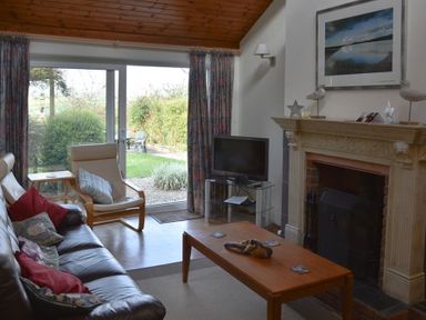 A living room with a brown leather sofa armchair wooden coffee table fireplace and glass doors leading to a garden at Gellifor in St Dogmaels Pembrokeshire