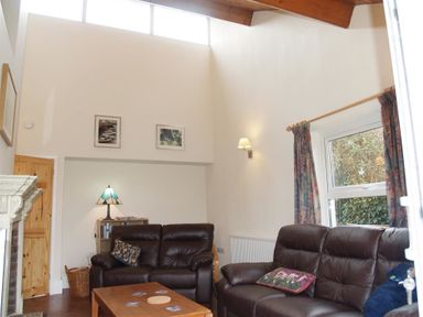 A living room with two brown leather sofas a wooden coffee table a window with curtains and wall lights at Gellifor in St Dogmaels Pembrokeshire