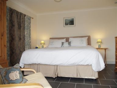 A bedroom with a bed two bedside tables with lamps a wooden wardrobe and a chair with a rabbit cushion at Gellifor in St Dogmaels Pembrokeshire