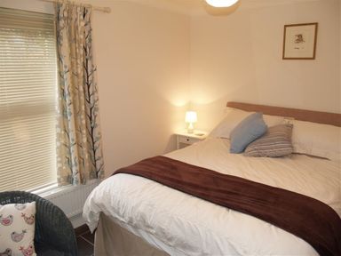 A bedroom with a bed pillows bedside table lamp window with curtains and a chair at Gellifor in St Dogmaels Pembrokeshire