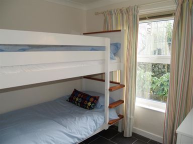 A bedroom with white bunk beds and a window with striped curtains at Gellifor in St Dogmaels Pembrokeshire