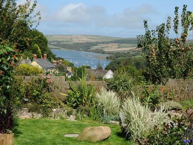 A garden with grass large rock and various plants overlooking a river mouth hills houses and boats in the distance at Gellifor in St Dogmaels Pembrokeshire