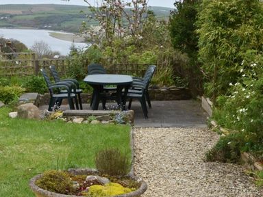 An outdoor patio area with a round table and six chairs surrounded by garden plants and overlooking a river and hills at Gellifor in St Dogmaels Pembrokeshire