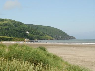 A sandy beach with grassy dunes and green hills in the background at Gellifor in St Dogmaels Pembrokeshire