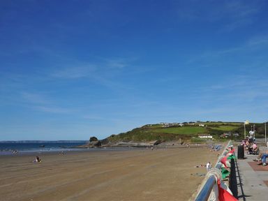 A sandy beach with people on it and a promenade with benches and flags at Seabrook Broad Haven Pembrokeshire