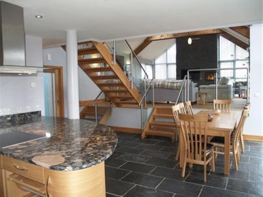 A kitchen with a black granite countertop adjacent to a dining area with wooden table and chairs and stairs leading to a raised living room at Seabrook in Broad Haven Pembrokeshire
