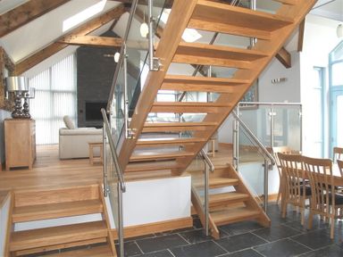 A wooden staircase with glass railing in an open living and dining area with wooden furniture at Seabrook in Broad Haven Pembrokeshire